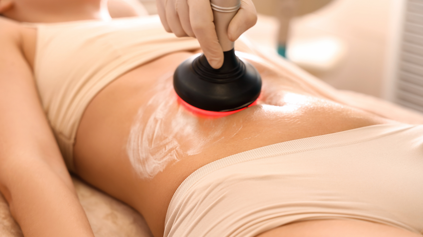 Person receiving a body treatment with a red light device applied to the abdomen, in a medical setting.