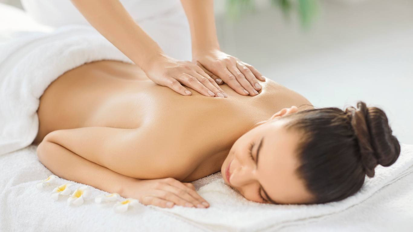 Person receiving a back massage at a spa. Hands apply pressure on bare back; eyes closed.