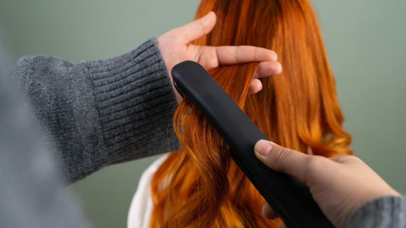 Hands curling red hair with a black flat iron.