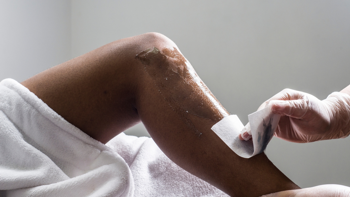 Leg being waxed; wax applied, strip being pulled by gloved hand in a spa setting.