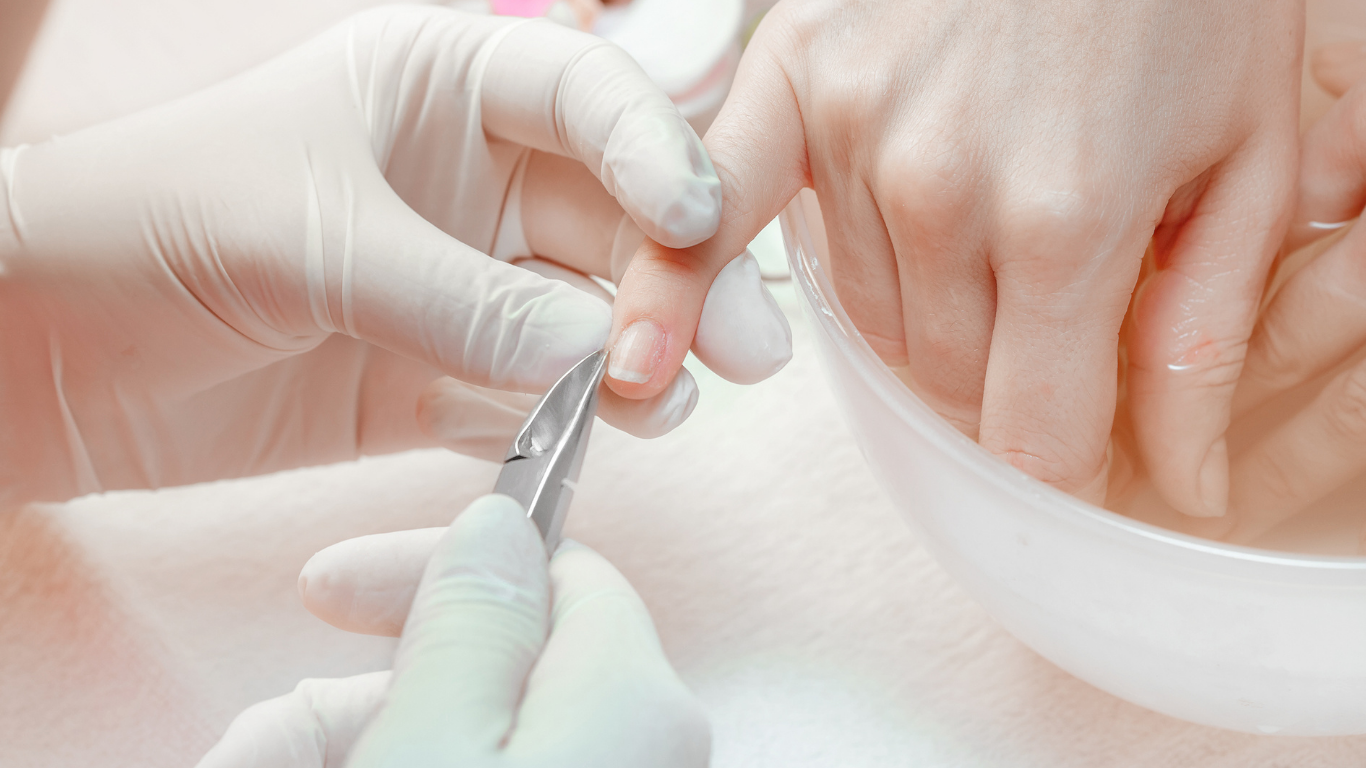 Manicurist trimming a fingernail with clippers; hand in water bowl.