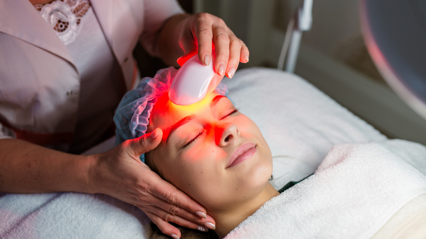 Woman receiving red light therapy on her face in a spa setting.