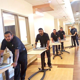 Men in black shirts and pants moving tables in a long hallway.