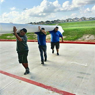 Three men carrying a large rolled-up white carpet outdoors near a red-painted curb.
