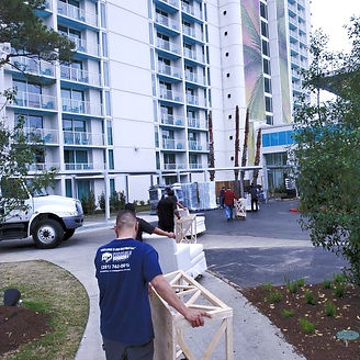 Movers unloading furniture in front of a tall, modern building with balconies and a driveway.