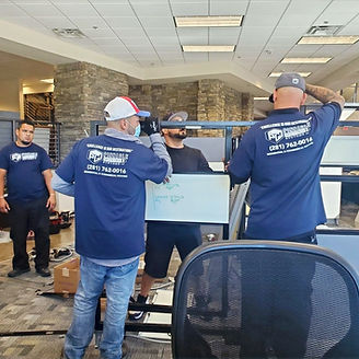 Four movers in blue shirts moving office furniture. Whiteboard and desk chair in foreground.