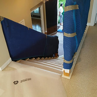 Staircase with protective padding. Moving crew member in background; carpeted steps with blue padding.