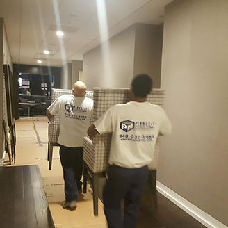 Two movers carrying armchairs down a hallway; moving service logo on their shirts.