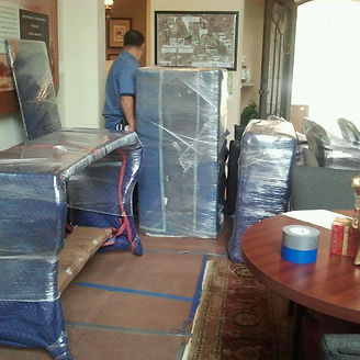 Man moving furniture wrapped in blue plastic, inside a room.