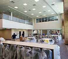 Large, open room with tables covered in plastic; people moving furniture.
