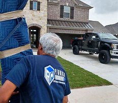 Person in blue shirt moving a wrapped object, house and black truck in background.