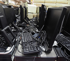 A cluttered array of black computer monitors, keyboards, and cables, likely discarded.