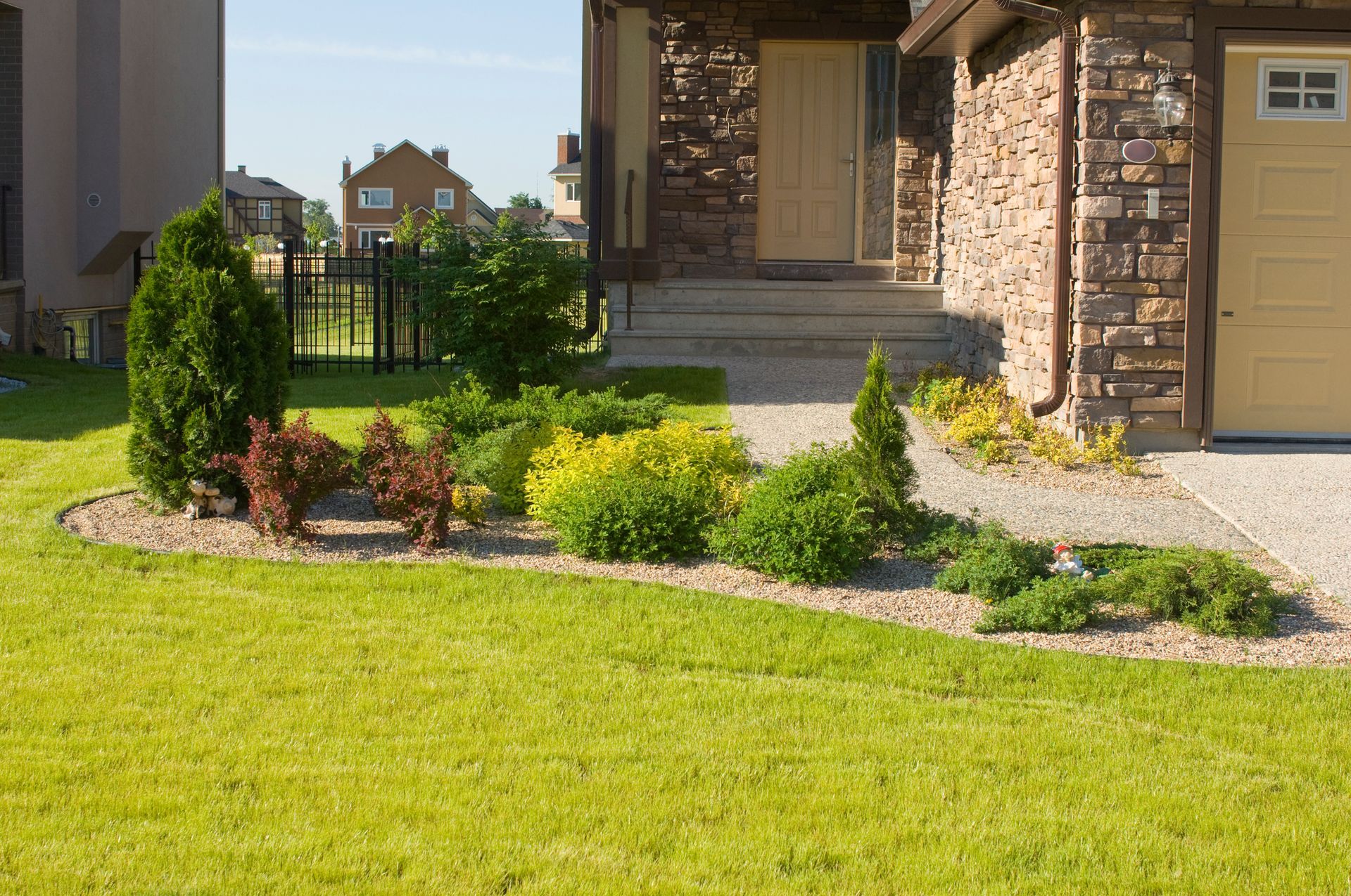 House with brick driveway, green lawn, tall trees, and blue sky.