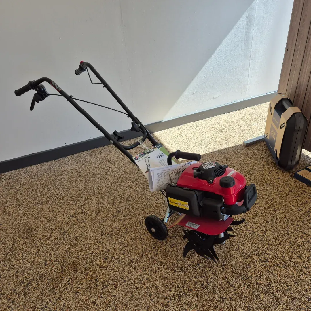 Rød og sort rorkult på brunt spættet gulv, mod en hvid væg og et brunt træpanel.