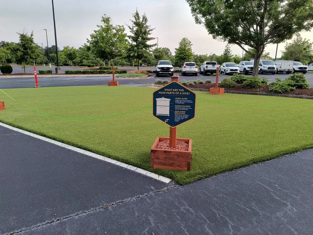 Newly sodded lawn with a small sign at the corner of a parking lot and road, bordered by orange cones.