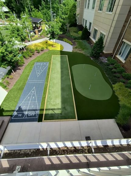 Overhead view of a backyard lawn game setup with two shuffleboard lanes and a putting green area