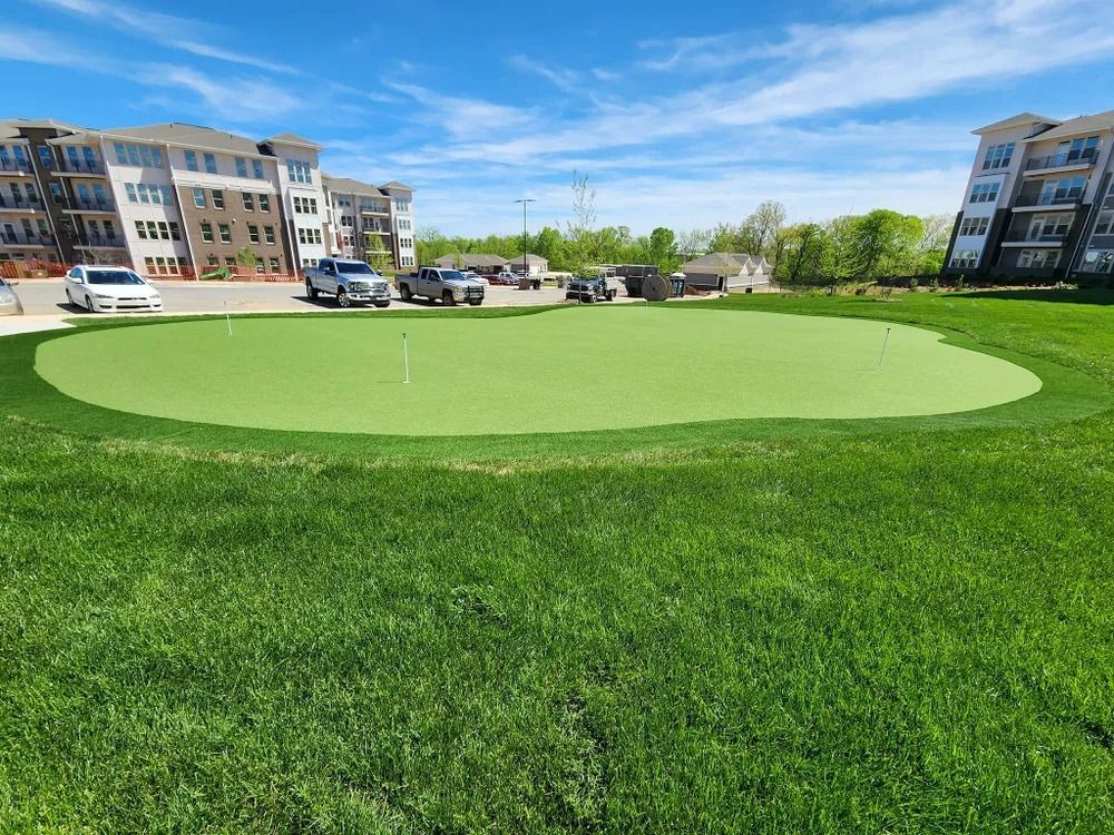 Green golf putting area in a residential courtyard with apartment buildings and parked cars nearby
