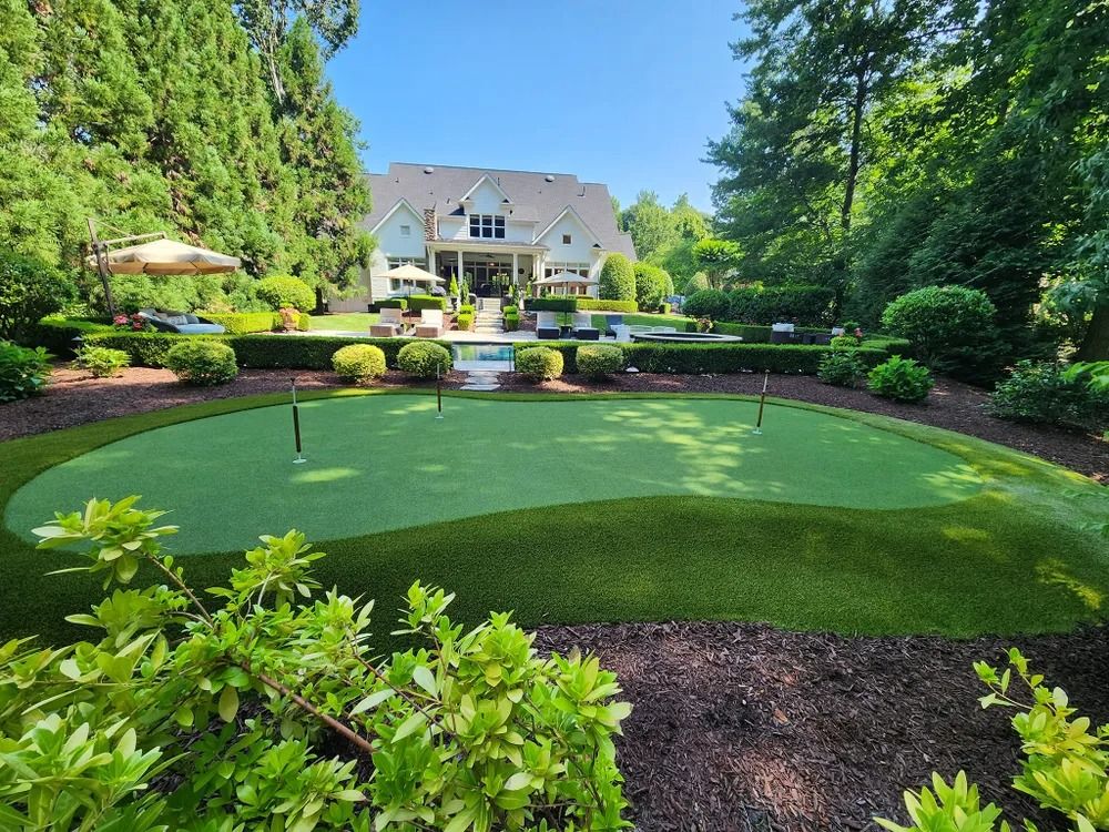 Manicured backyard putting green with lush landscaping and a large house in the background