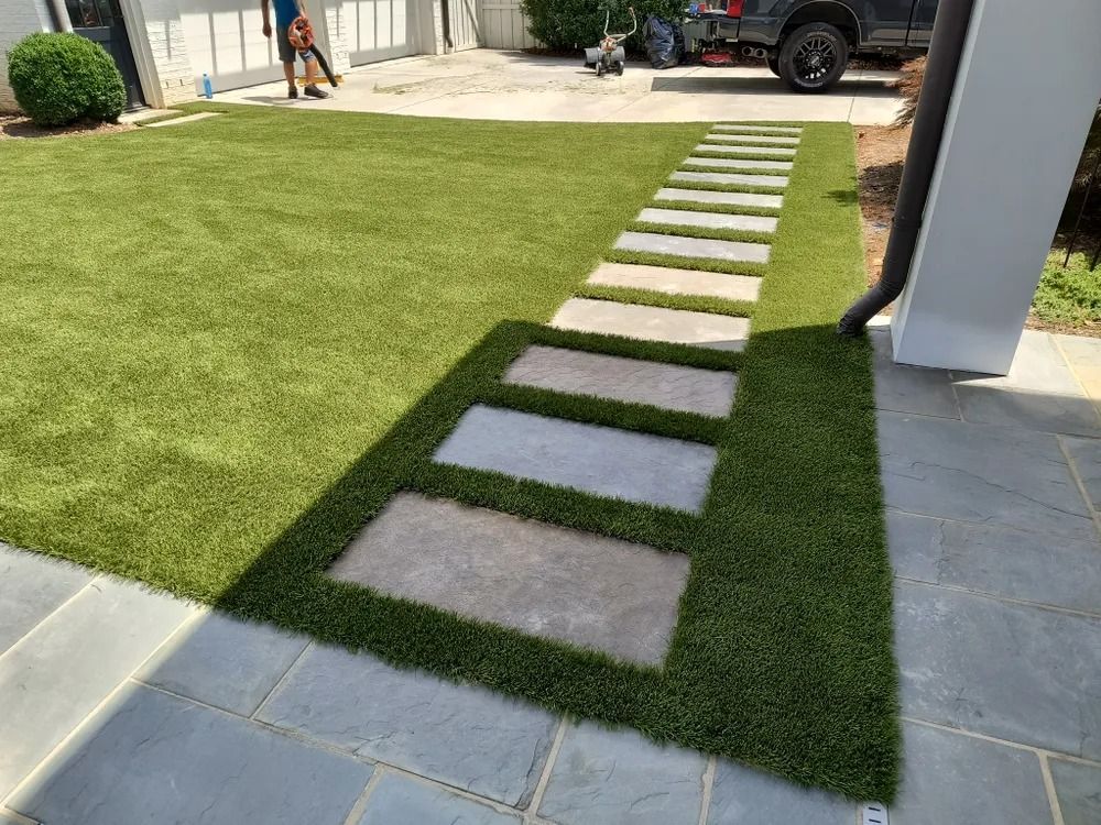 Stepping stones set in a narrow grass path beside a patio and driveway.