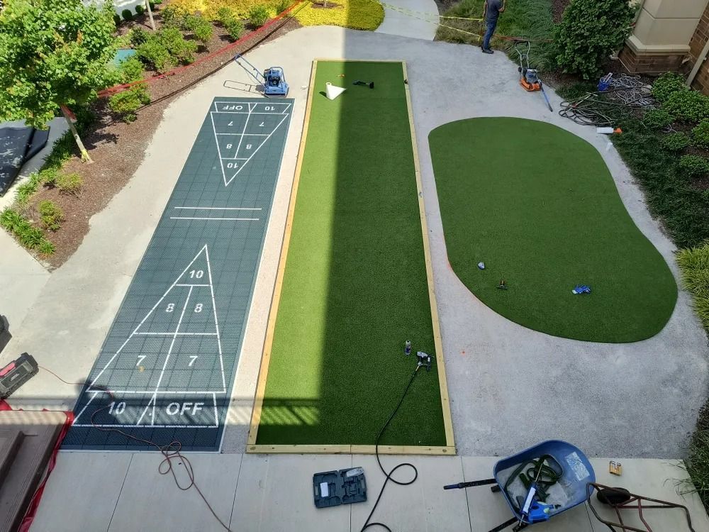 Overhead view of a backyard bocce court with two green lanes, concrete paths, and landscaping.