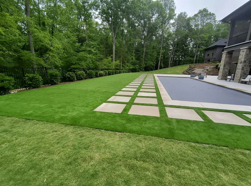 Stone walkway beside a patio and lawn, bordered by trees in a landscaped backyard
