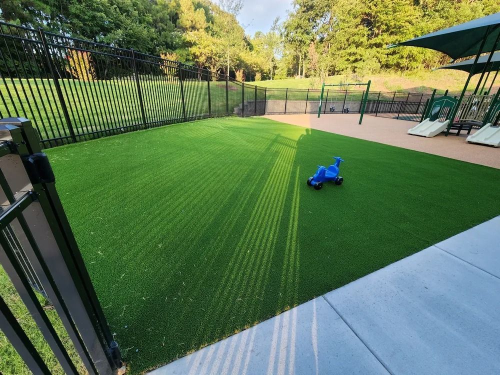 Backyard patio with artificial turf, black fence, lounge chairs, and a blue toy on the grass