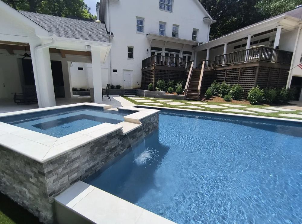 Blue swimming pool with a raised hot tub beside a white house and covered patio