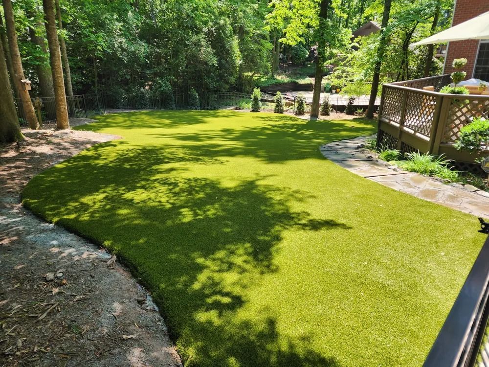 Artificial turf lawn with trees, stone path, and wooden deck in a sunny backyard