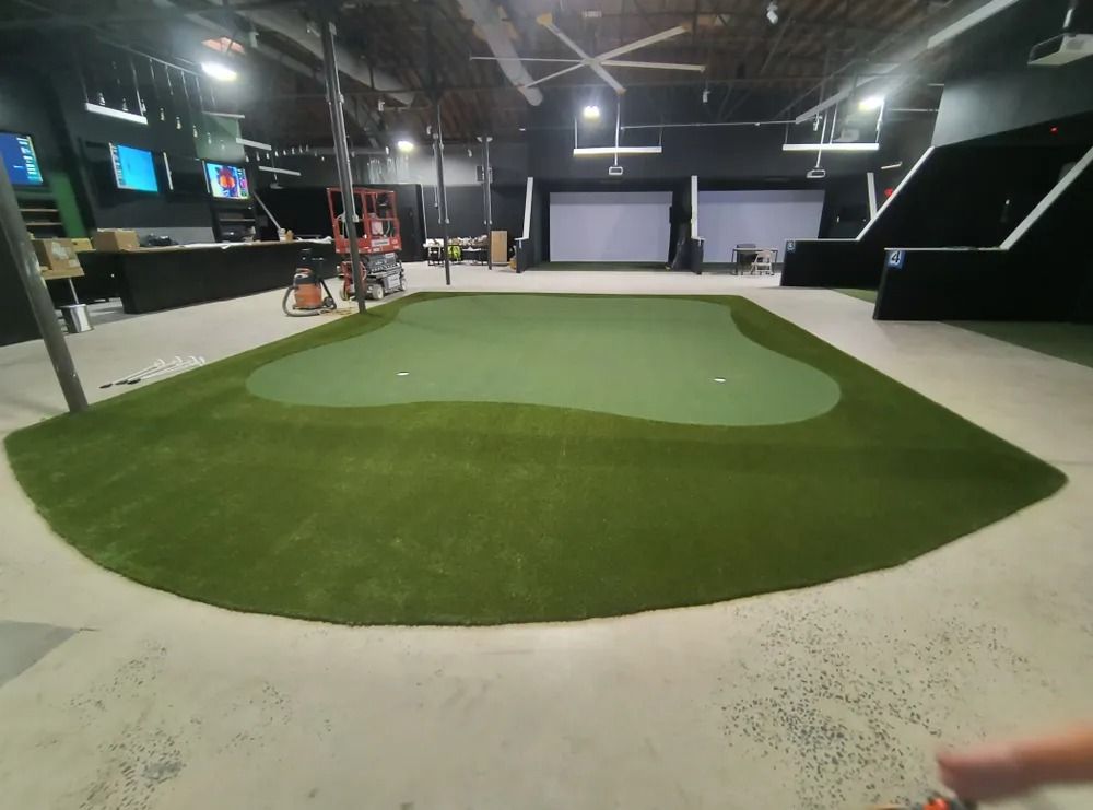 Indoor golf simulator bay with green turf putting area and large projection screen