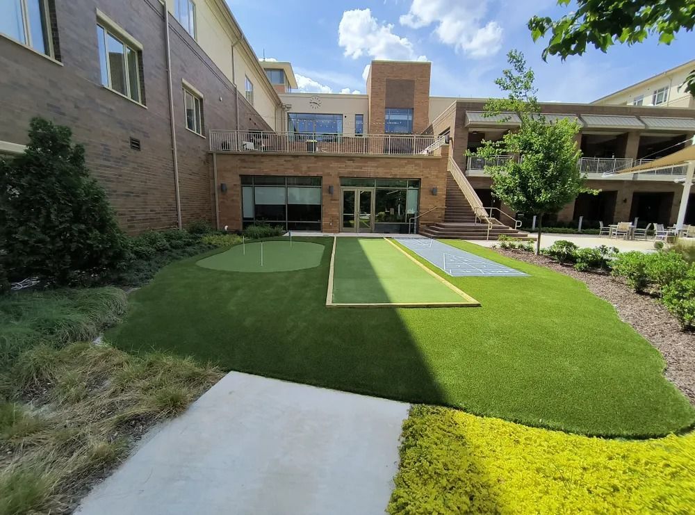 Courtyard with artificial turf, concrete paths, brick buildings, and a stairway under a partly cloudy sky