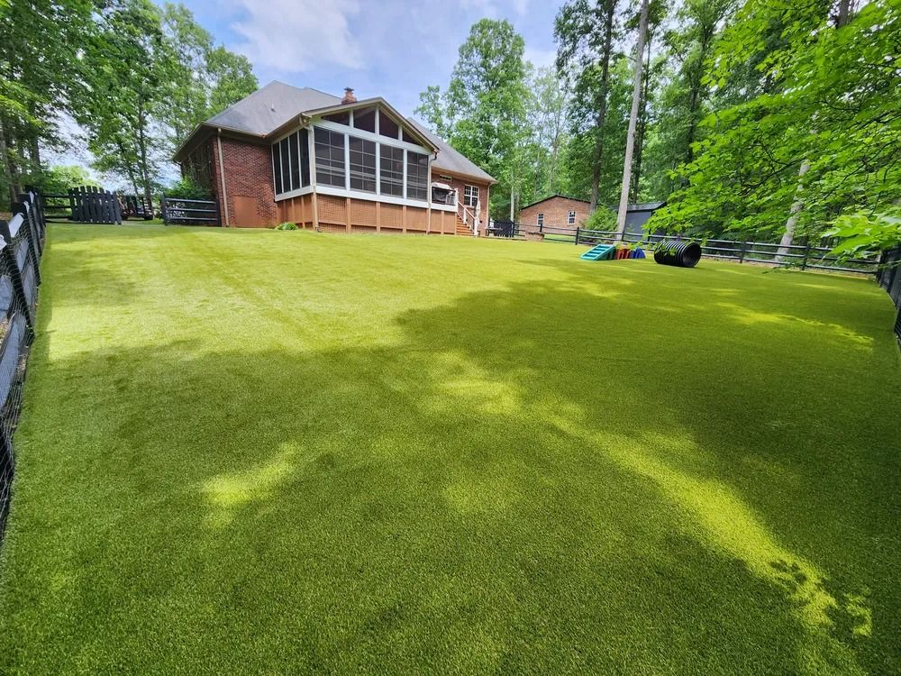 Wide green lawn leading to a brick house with large windows and trees around it