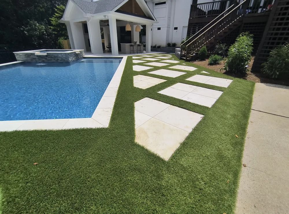 Backyard poolside path with white stone pavers set in green grass beside a blue swimming pool