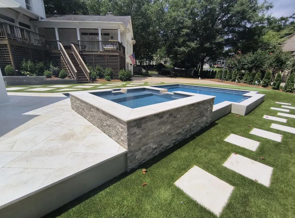 Modern backyard with blue-tiled pool, stone hot tub, and stepping stones on a lawn.