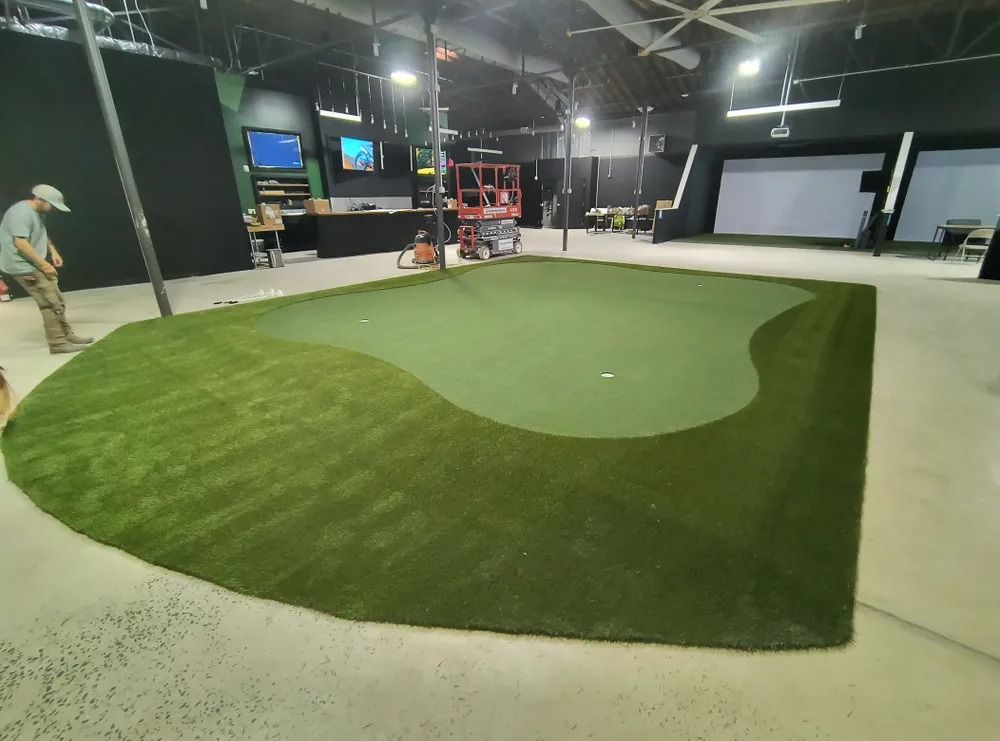 Indoor golf putting green with two people practicing under bright lights