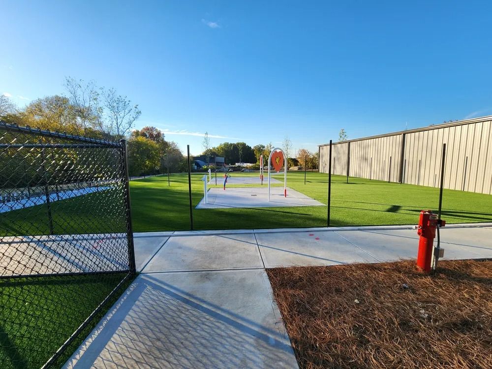 Outdoor park path leading to a fenced concrete court, with a red hydrant and long wooden fence on the right.