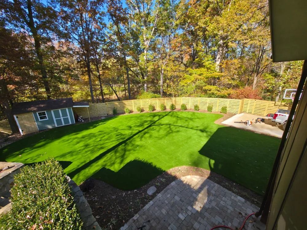Backyard with bright green lawn, stone patio, shed, and autumn trees in sunlight