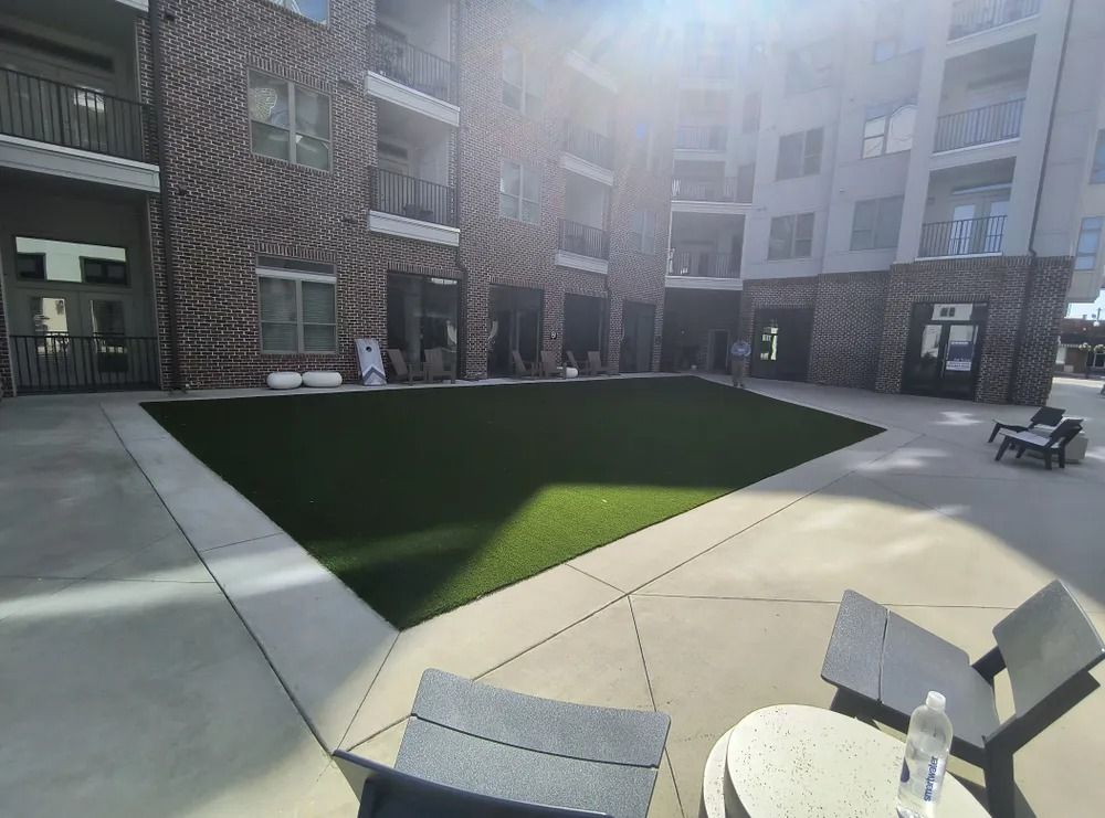 Apartment courtyard with a sunlit rectangular lawn, patio chairs, and surrounding brick buildings