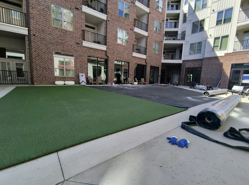 Courtyard with green turf, apartment buildings, and a concrete patio with a hose and blue toy on the ground