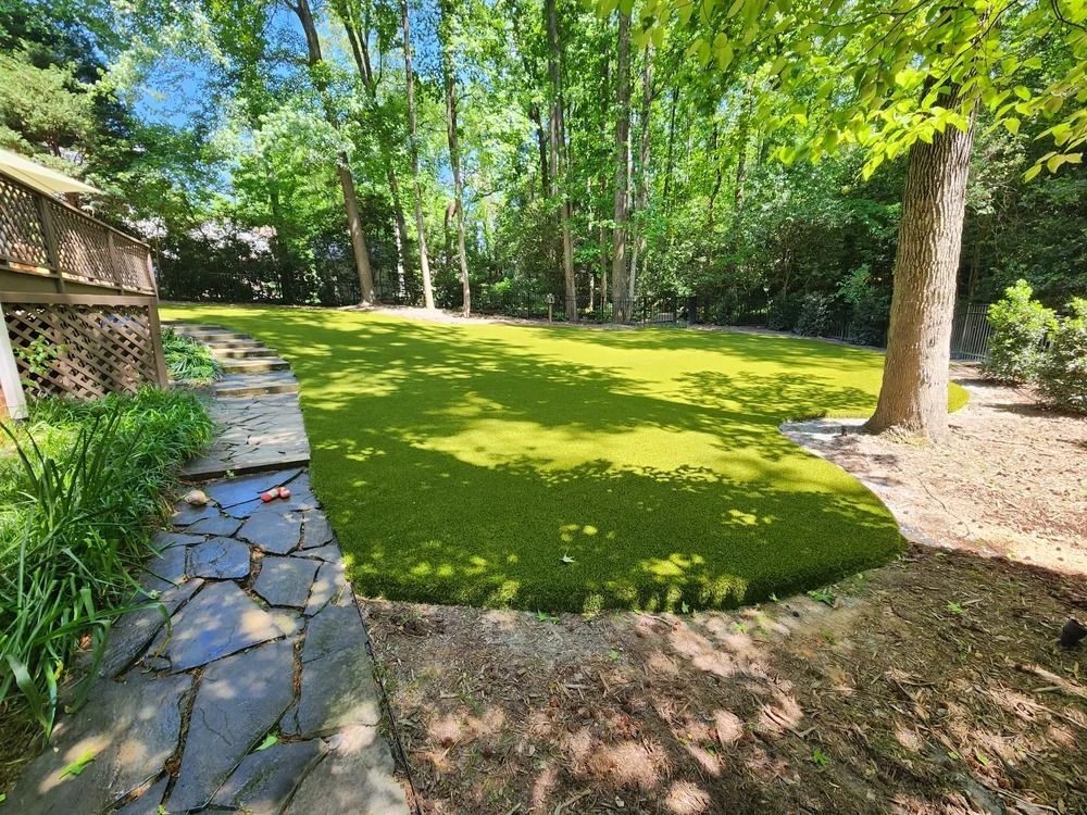Sunlit backyard with green lawn, stone path, and trees beside a house