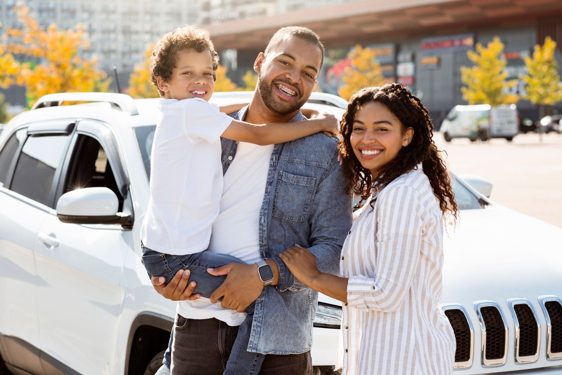 Family smiling beside white SUV in a sunny parking lot