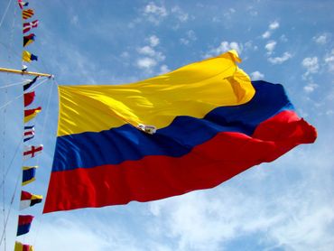 Colombian flag waving against a blue sky with scattered clouds