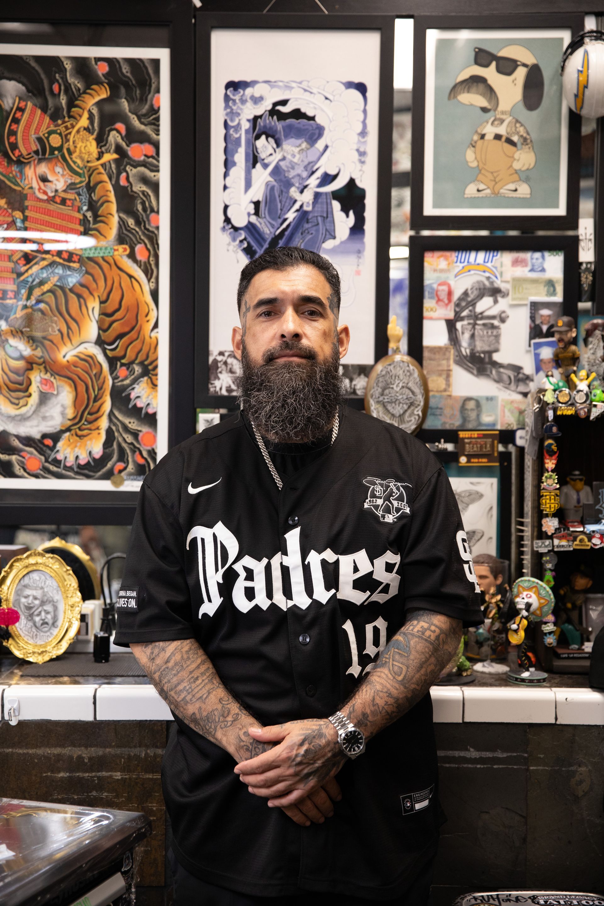 Man standing in a Padres jersey in front of framed artwork and collectibles in a tattoo shop