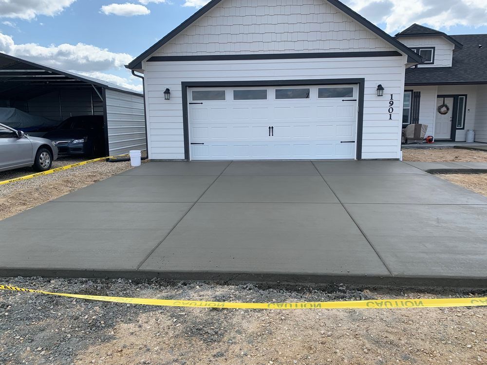 A car is parked in front of a garage with a concrete driveway.