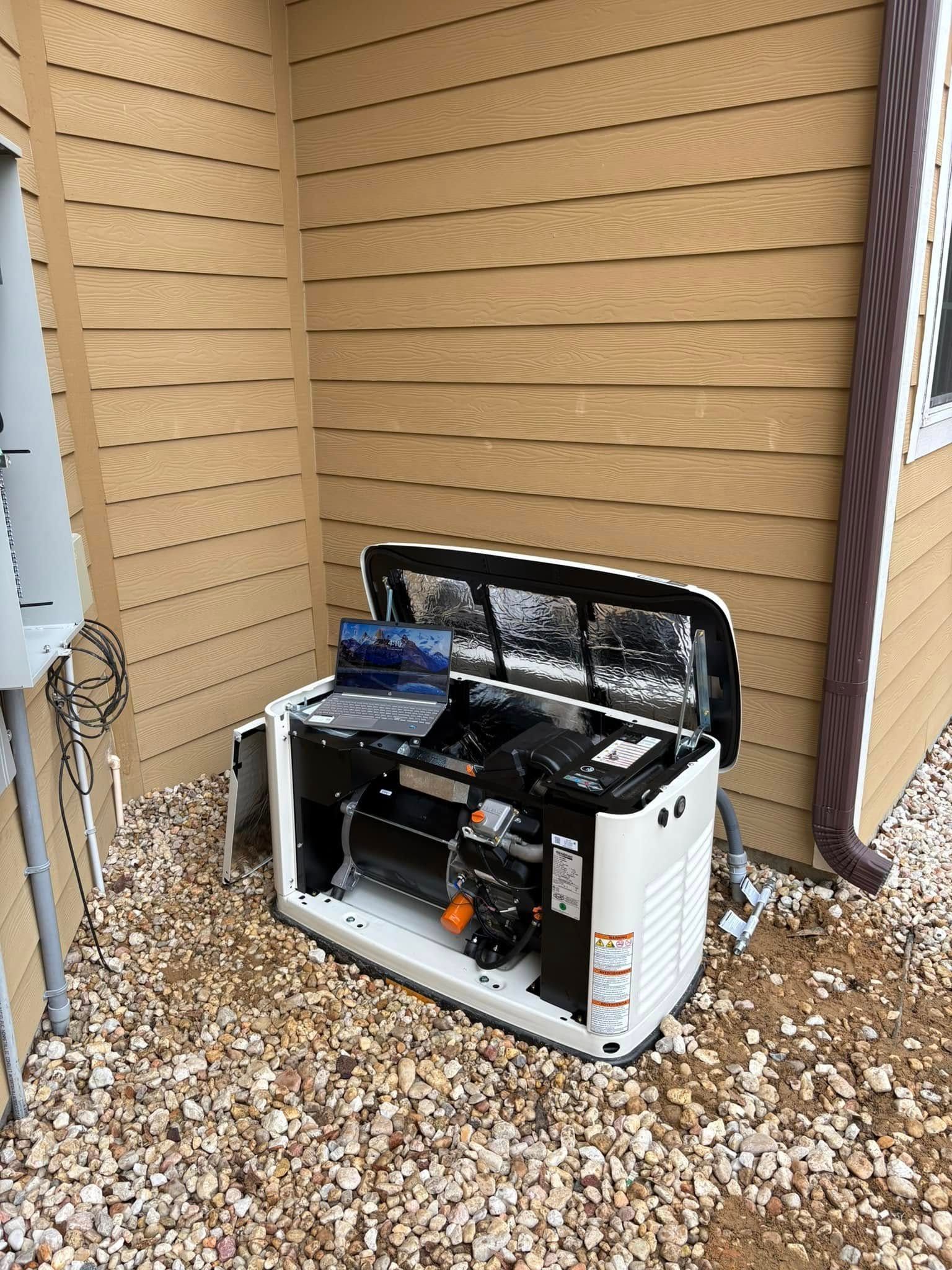 Outdoor generator with open top, next to a house with tan siding, on a bed of gravel.