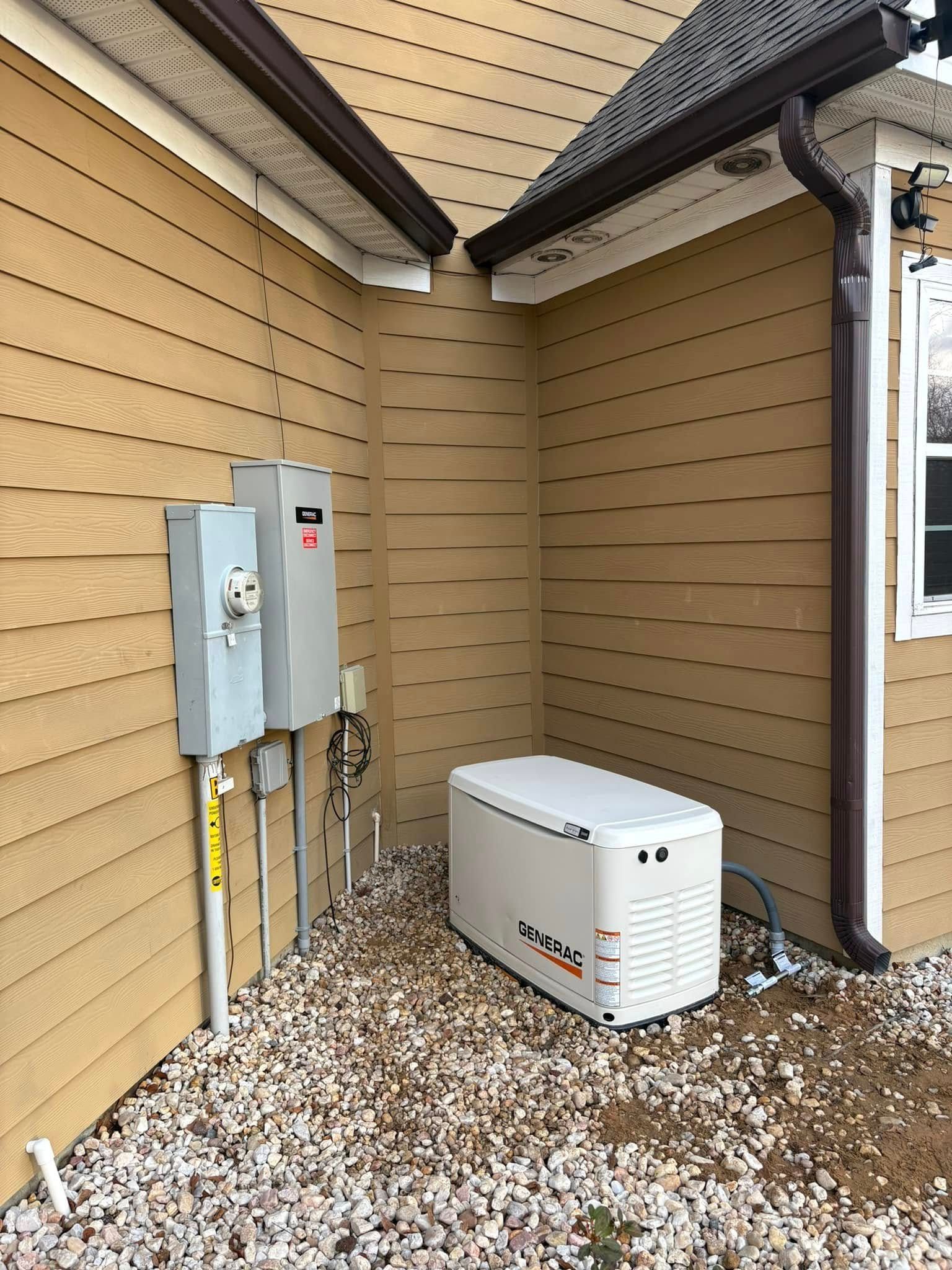 Generator and electrical boxes installed outside a home, near siding and gravel.