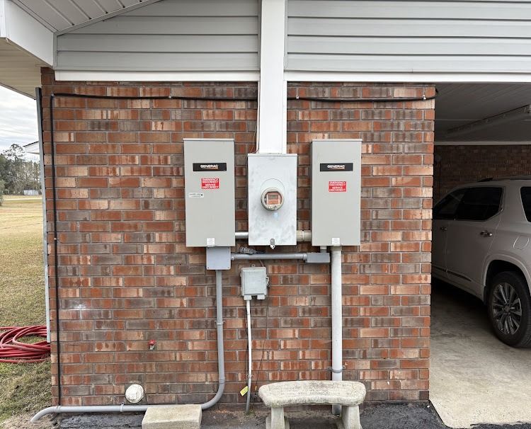 Electrical boxes on a brick wall, with a meter, under a carport, grey boxes and conduit.