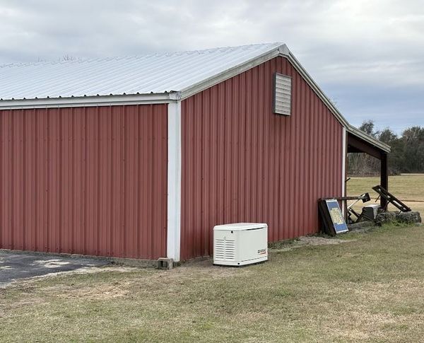 Red barn with white trim, metal roof, and a generator outside on the grass.