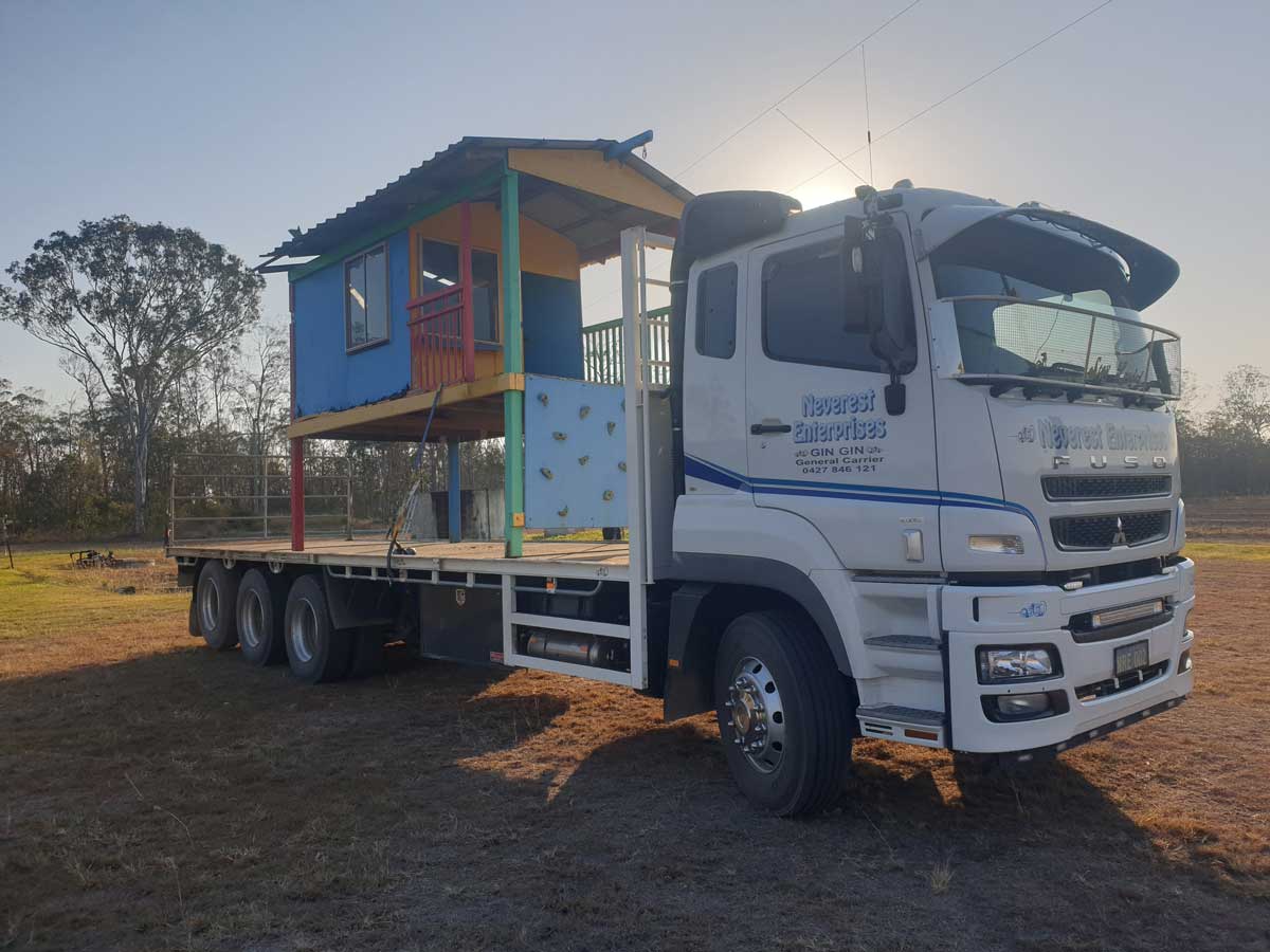 A white truck is carrying a colorful playhouse on a flatbed trailer.