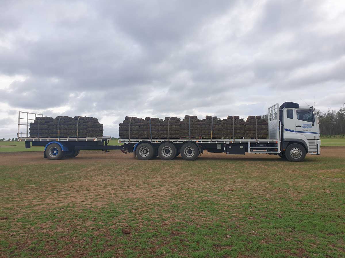 A truck with a trailer full of hay is parked in a field.