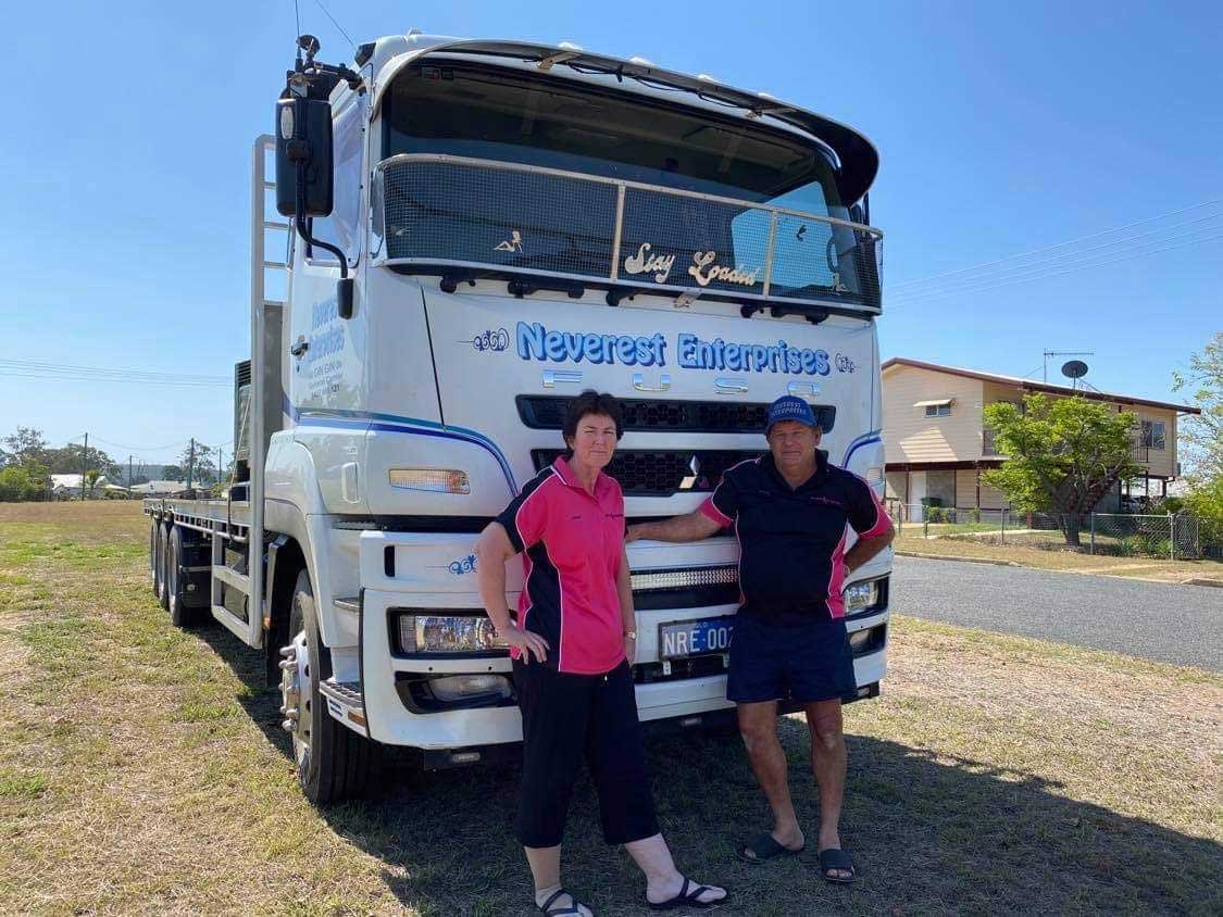A man and a woman are standing in front of a truck.